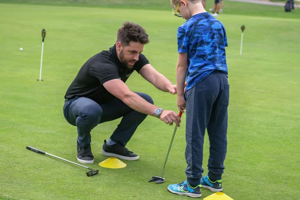 Golf coach helping a young boy with putting on the practice green at The Shropshire Golf Club in Telford, part of junior golf lessons in Telford