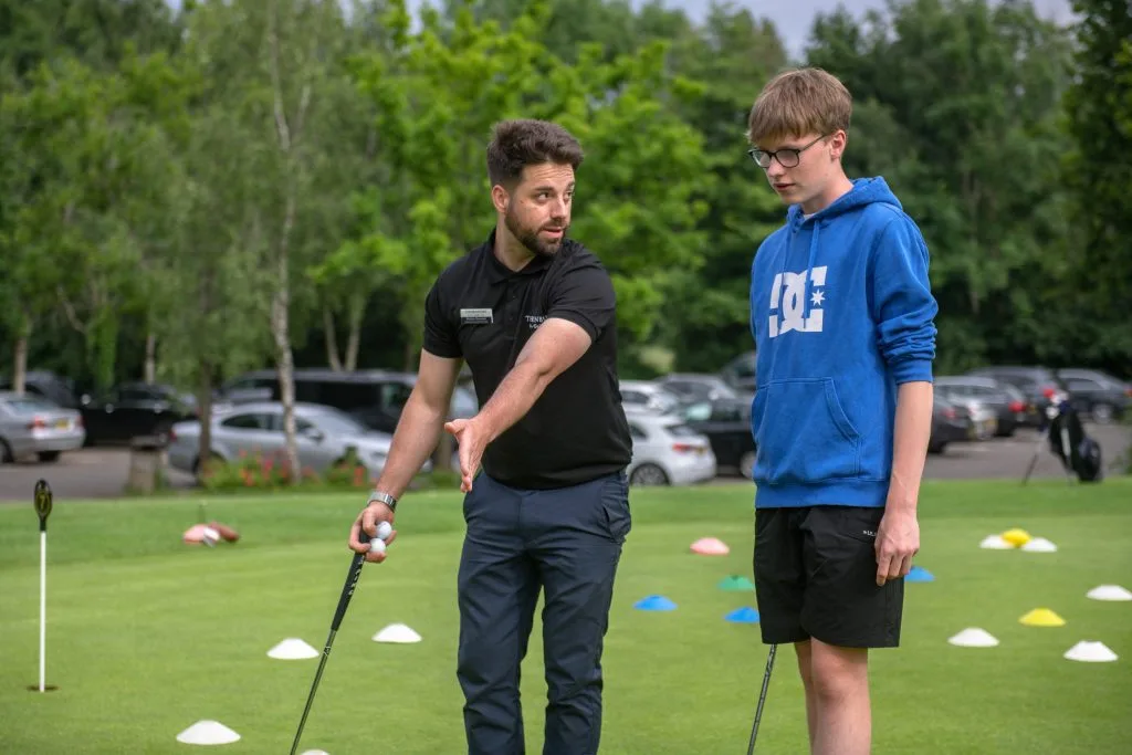 Golf coach assisting a teenager with swing technique at The Shropshire Golf Club in Telford, part of youth golf coaching and golf lessons in Telford